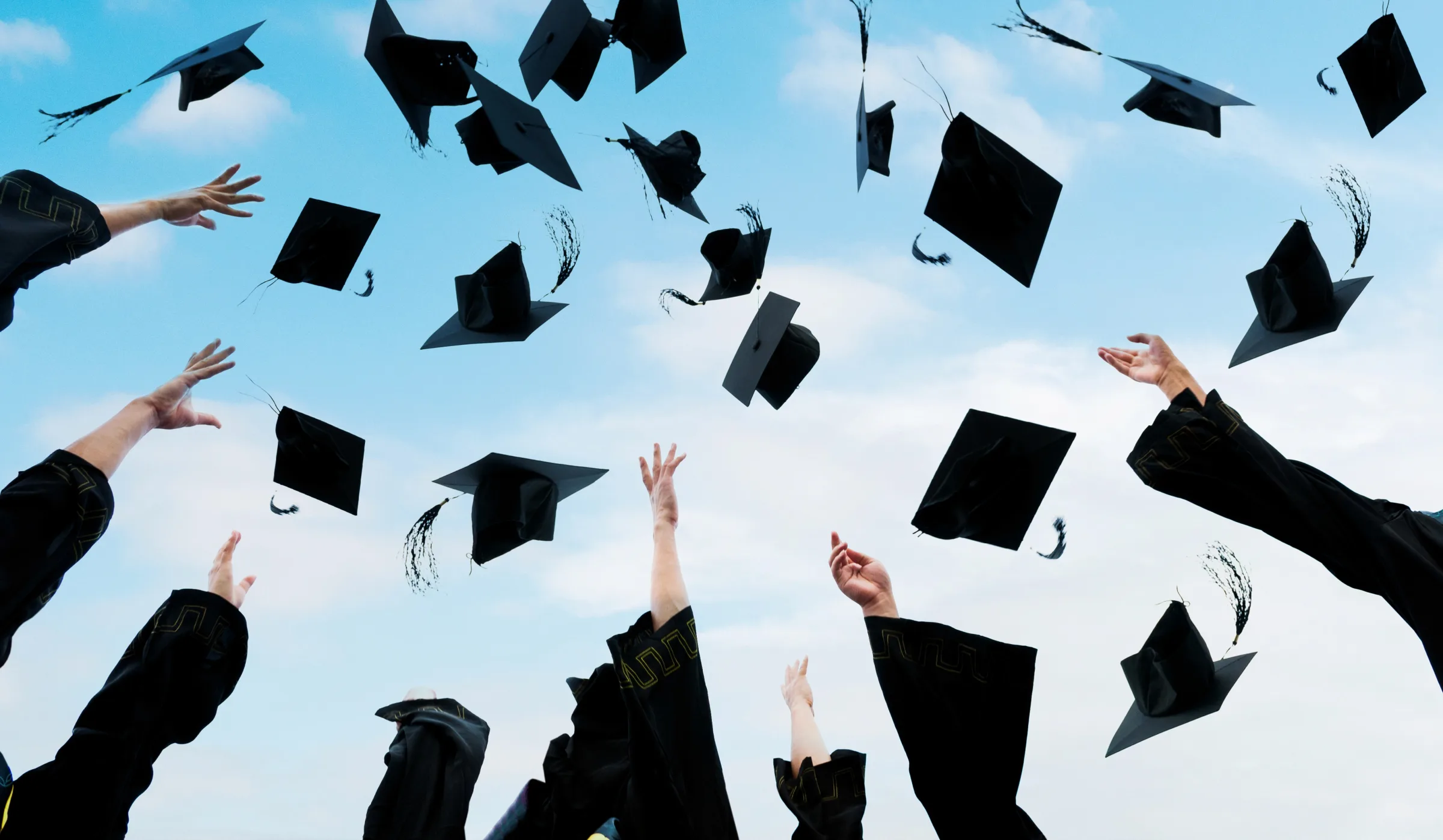 Graduates throwing mortarboard caps into a blue sky